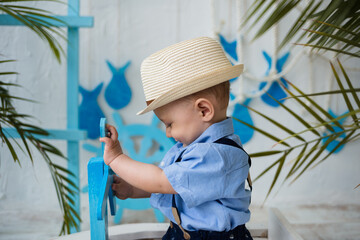 a kid in a straw hat sits in a wooden boat on a background with a sea decor