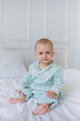 baby boy in striped pajamas sits on the cotton bedding on the bed and looks at the camera