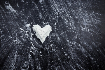 Scattered white flour with heart shape on black surface.