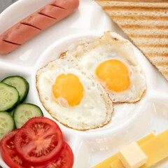 Classic American Breakfast. Two fried Eggs, sausage, cheese, toast and salad on white portion plate. High angle view. Square format for web banner. Close up shot.