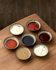 Obraz na płótnie Canvas Set of different multi-colored sauces in crockery on wooden table. Variety of sauces, mayonnaise, mustard, soy sauce, ketchup, Side top view. Copy space.