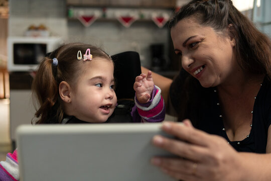 Child With Physical Disability Playing With Mother And Digital Tablet In The Kitchen. .