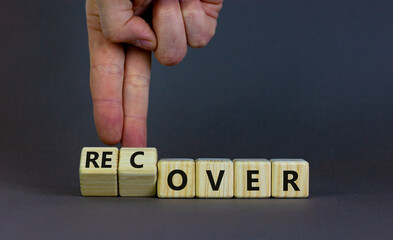 Time to recover symbol. Businessman turns wooden cubes and changes the word 'over' to 'recover'. Beautiful grey table, grey background. Business, over or recover concept. Copy space.