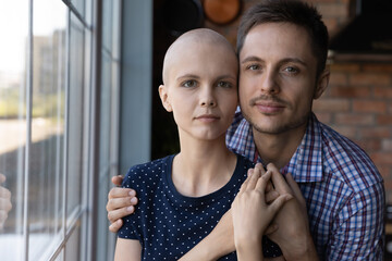 Married young couple fighting against woman oncology disease. Husband hugging hairless ill wife...