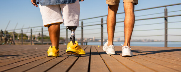 black man with prosthetic leg with friend walking in deck outdoors. - obrazy, fototapety, plakaty