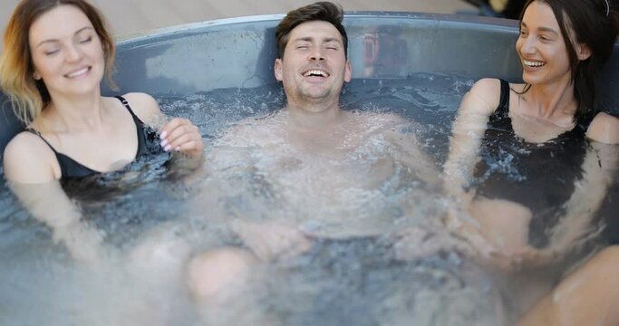 Man and women bathing in outdoor jacuzzi or hot vat at the luxury spa. Friends have fun and relax in wellness center