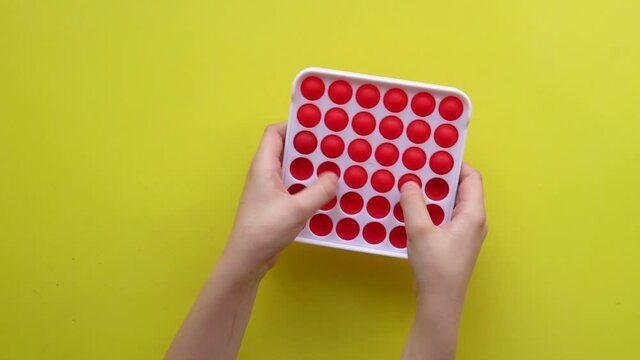 Popit antistress toy for children entertainment on a yellow background playing a child top view in colored fijit simple dimple popit yellow fun children, sensory color popular rt, modern trend. Hand