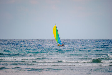 Scenic view at small catamaran with yellow green blue sail sailing in sea. Team of unrecognizable people enjoy together tropical sea. Small waves on turquoise surface, clean blue skies