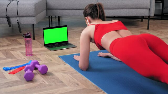 Mockup chroma key monitor laptop: Strong fitness woman in sportswear doing plank exercise workout on yoga mat looking green screen computer display. Fit girl training online video call webcam at home