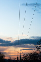Sylwetka słupa energetycznego na tle wieczornego nieba, na dalszym planie wieża kościelna