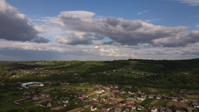 Aerial drone footage of countryside, road between fields and forest in cloudy weather. Rural area with small buildings on background mountains landscape. Travel destination for tourism and wanderlust
