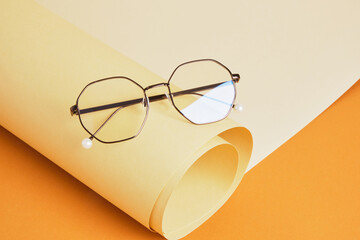 trendy eye glasses on rolled beige paper, geometric background, trending colors, yellow background