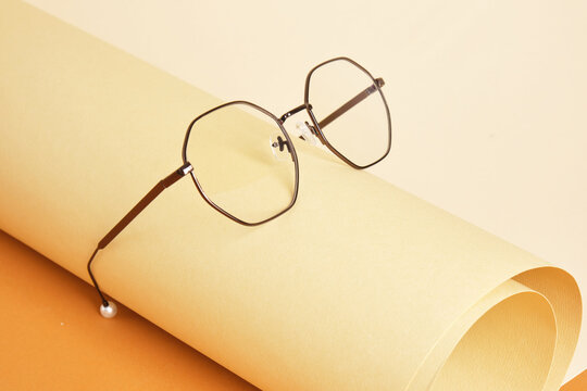 glasses on rolled beige paper, geometric background, trending colors, yellow background