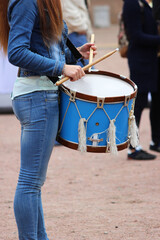 girl drummer with a big blue drum stands on the street and prepares to perform at the parade.