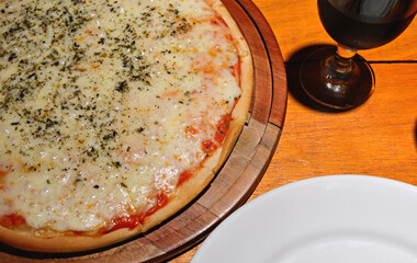 Rustic wooden table with close-up mozzarella pizza, a white plate and a glass of wine.