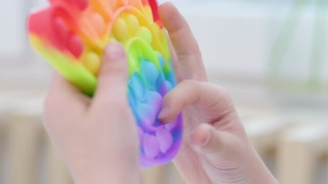 Child play with pop it sensory toy. Boy presses on colorful rainbow squishy soft silicone bubbles. Stress and anxiety relief. Trendy fidgeting game for stressed children and adults