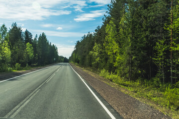 Fototapeta na wymiar The road among the Karelian taiga. Pine forest on the side of the road. Trip to Karelia. Highway among the trees. Driving on a trip to beautiful places. Karelia. Day.