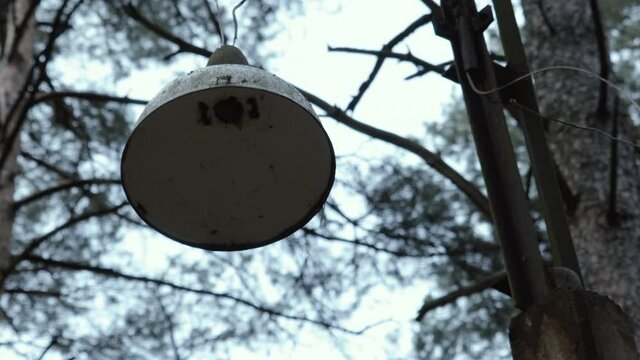 Single battered lantern dangles in the wind in an abandoned autumn park in cloudy weather. Concept of mysticism and thriller in a concentration camp