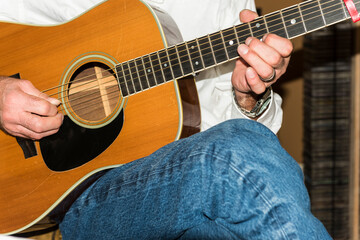 Detail of a man's hands playing an acoustic steal string guitar.