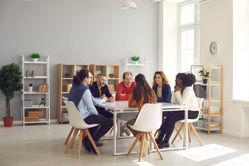 Team of mixed race business people sitting around big table in modern office space. Group of...