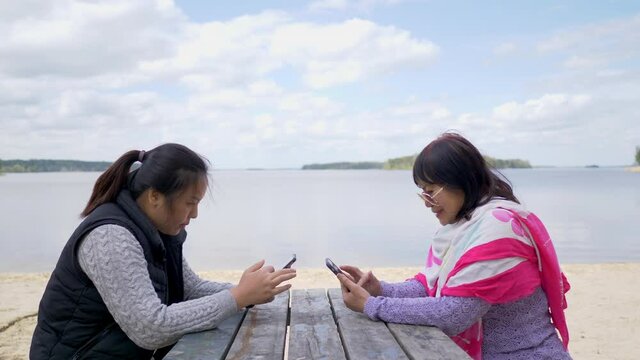 Asian smartphone addict adult mom and daughter using each other phone at the beach, slide the screen. No coversation during the trip. Social media addicted people