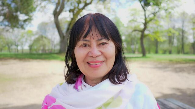 Close up outdoor portrait of a happy Asian old woman with straight hair and smile face. Standing at the park, getting some fresh air outside, relaxing and staying healthy