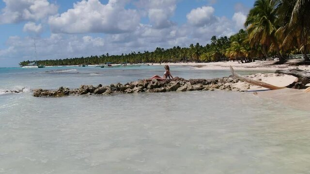 Young woman is sitting on the rocks at the beach, blue water, tropical vacation