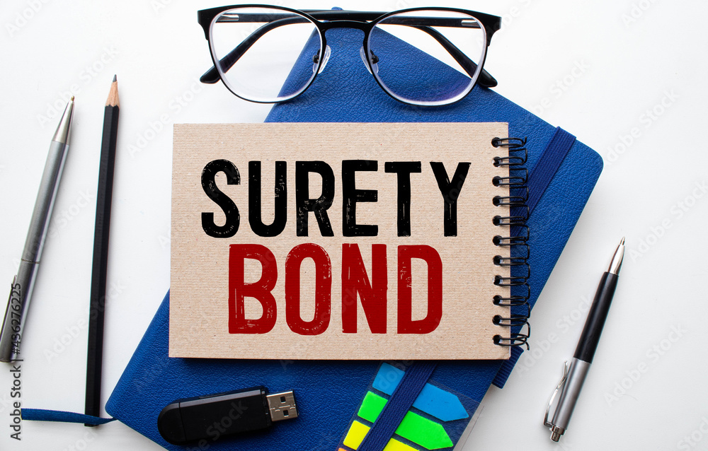 Poster text surety bond is written on a notebook with a pen and a magnifying glass lying on the table.