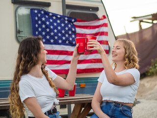 View of white girls clinking cups with the flag of the United States of America in the background