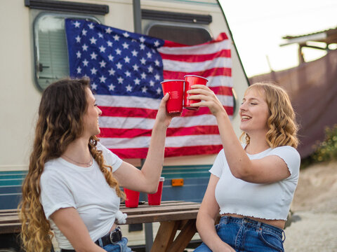 View of white girls clinking cups with the flag of the United States of America in the background