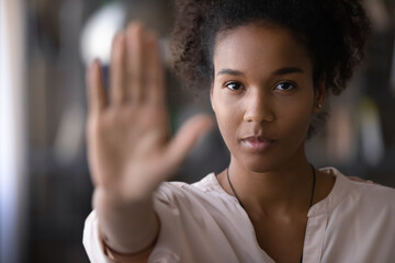 Head shot confident serious strong millennial generation african ethnicity woman looking at camera showing stop sign, denying abuse or bullying, protesting against racial or gender discrimination.