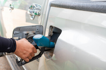 The hand is holding the nozzle to refuel the car in the gas station.