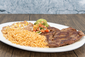 Carne Asada steak cooked to perfection and served with rice and beans on a plate.