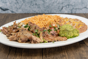 Shredded carnitas pork cooked to perfection and served with rice and beans on a plate