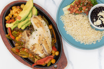 Overhead view of seafood fajitas plate with large grilled fillet on top of veggies and shellfish