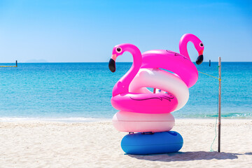 Fantasy Swim Ring and inflatable  flamingo balloon on the  sandy beach with blue sky and sea