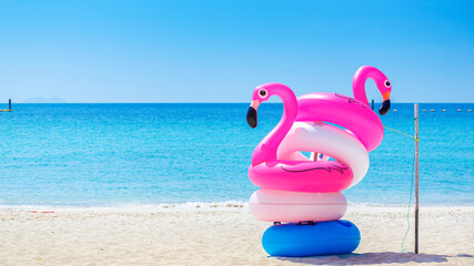 Fototapeta na wymiar Fantasy Swim Ring and inflatable flamingo balloon on the sandy beach with blue sky and sea