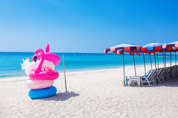Fototapeta na wymiar Fantasy Swim Ring and inflatable flamingo balloon on the sandy beach with blue sky and sea
