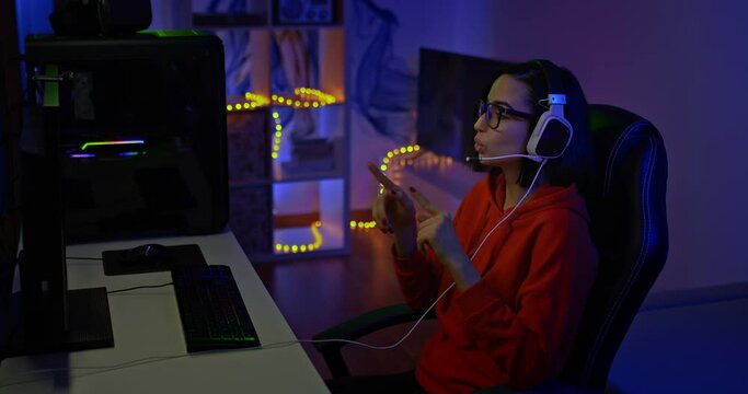 Young beautiful woman leads a conference on the network, online meeting. Woman blogger sits at a computer monitor in a dark room, she gestures and speaks. 4k, ProRes