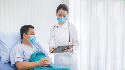 Asian professional woman doctor talking with a man patient who he is on bed about his pain and symptom in hospital. They wear a medical face mask to protect respiration system (Covid-19).