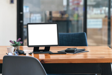 Mockup blank screen tablet with stand holder and gadget on wooden table in co-workspace.