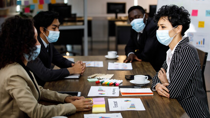 Multiracial smart formal businesspeople sitting face to face meeting and making group discussion at office, wearing face masks as new normal to protect or prevent virus in outbreak pandemic crisis.