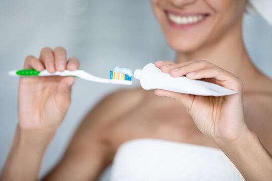 Happy woman brushing teeth with toothy smile, squeezing mineral mint toothpaste on plastic toothbrush, taking care about fresh breath and caries prevention. Hygiene, dental care concept. Close up