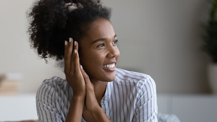 Head shot young african american authentic attractive woman with white toothy smile looking in distance, daydreaming or visualizing future, feeling joyful relaxing at home, natural beauty concept.