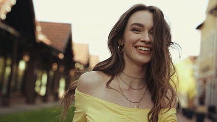 positive young woman with wavy hair smiling outside.