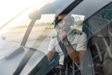 Young pilot is getting in his helicopter and preparing to take off. He is in his uniform and wearing sunglass.