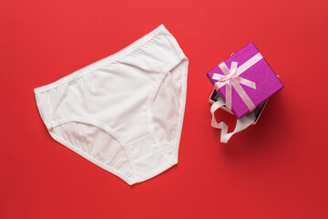 White women's underwear and a gift box on a red background. Flat lay.