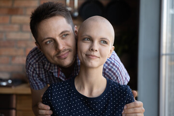 Happy young couple fighting against woman cancer, hugging at home, looking away, smiling, thinking,...