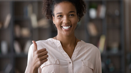 Happy candid authentic african american biracial attractive woman showing thumbs up gesture, smiling mixed race female client feeling satisfied, recommending product or evaluating service indoors. - Powered by Adobe