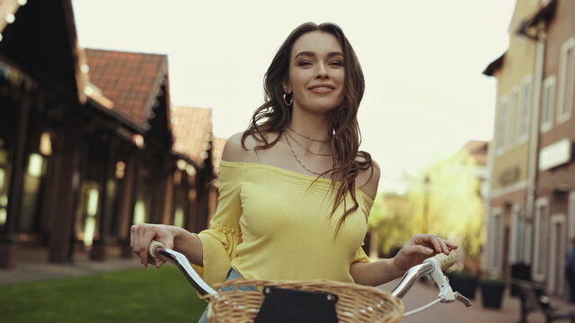 Happy Young Woman With Wavy Hair Smiling While Cycling Outside.